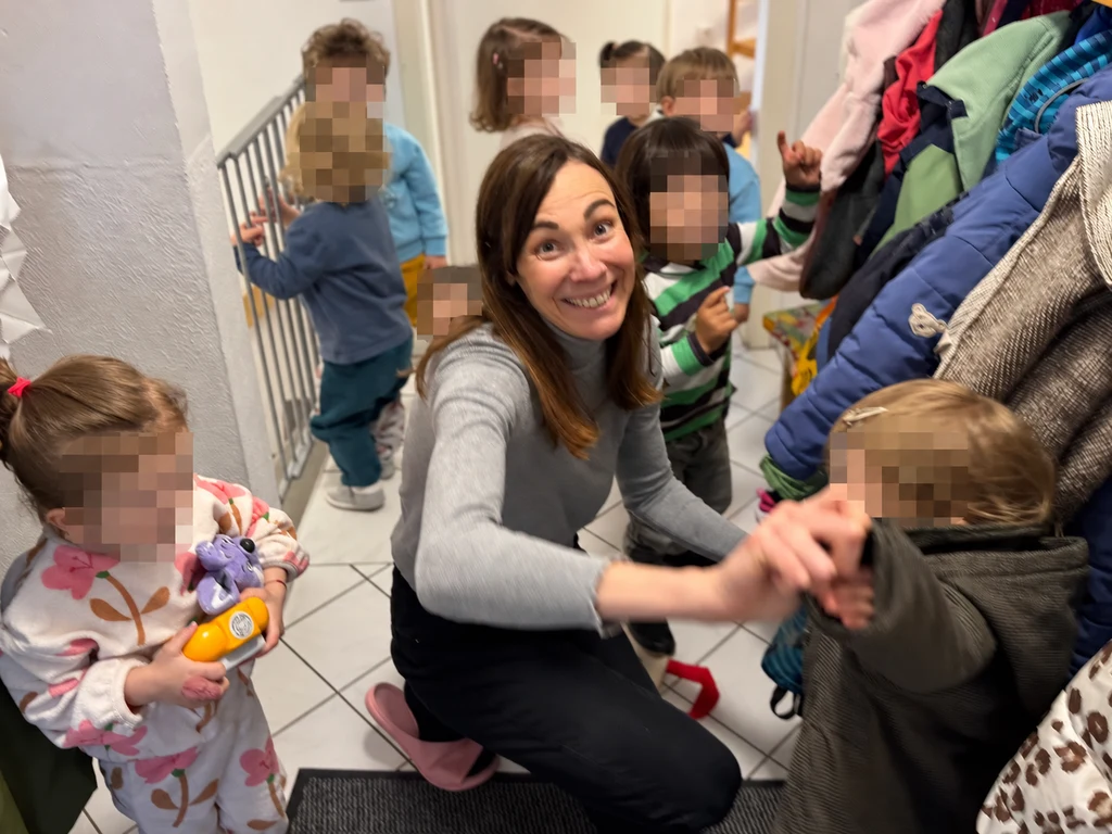 Hélène Duval mit Kindern im Eingangsbereich der Großtagespflege Fuchsbau in Unterhaching; die Gesichter der Kinder sind verpixelt