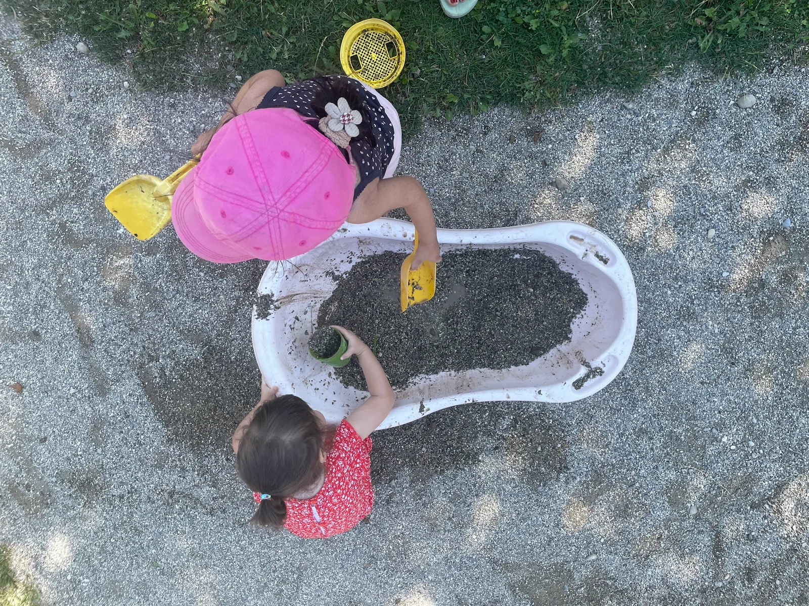 Zwei Kinder spielen mit Schaufeln und Bechern im Kies