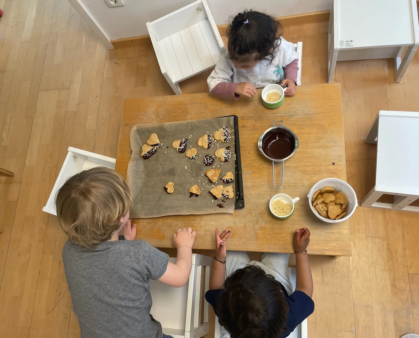 Kinder verzieren gemeinsam Plätzchen mit Schokolade und Streuseln